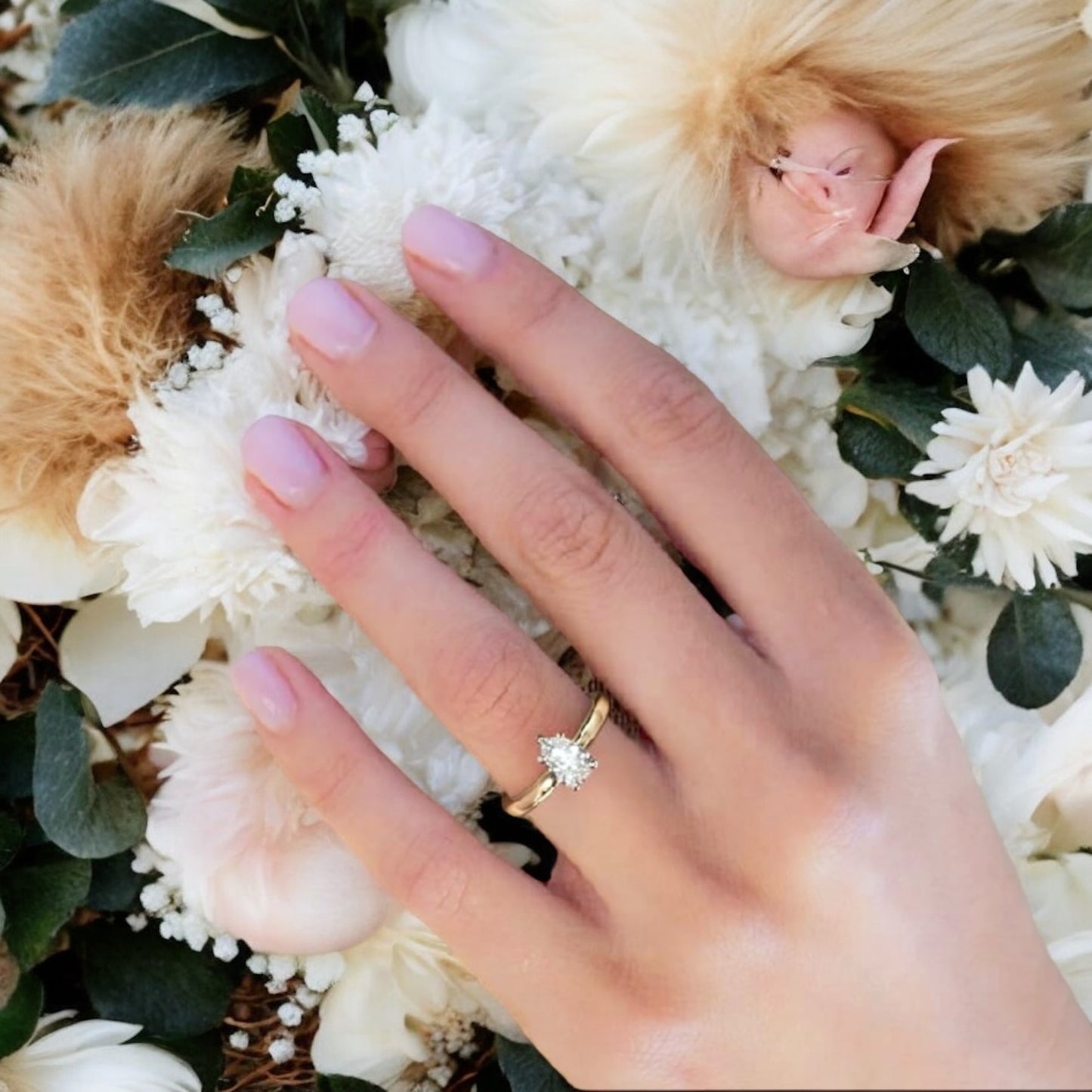 Elegant hand with IGI certified 1ct pear shape D color diamond VVS1 VVS2 3EX ring on finger surrounded by white flowers